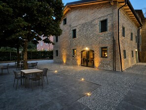 Un edificio de piedra con un patio, asientos al aire libre y un árbol.