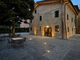 Un edificio de piedra con un patio, asientos al aire libre y un árbol.