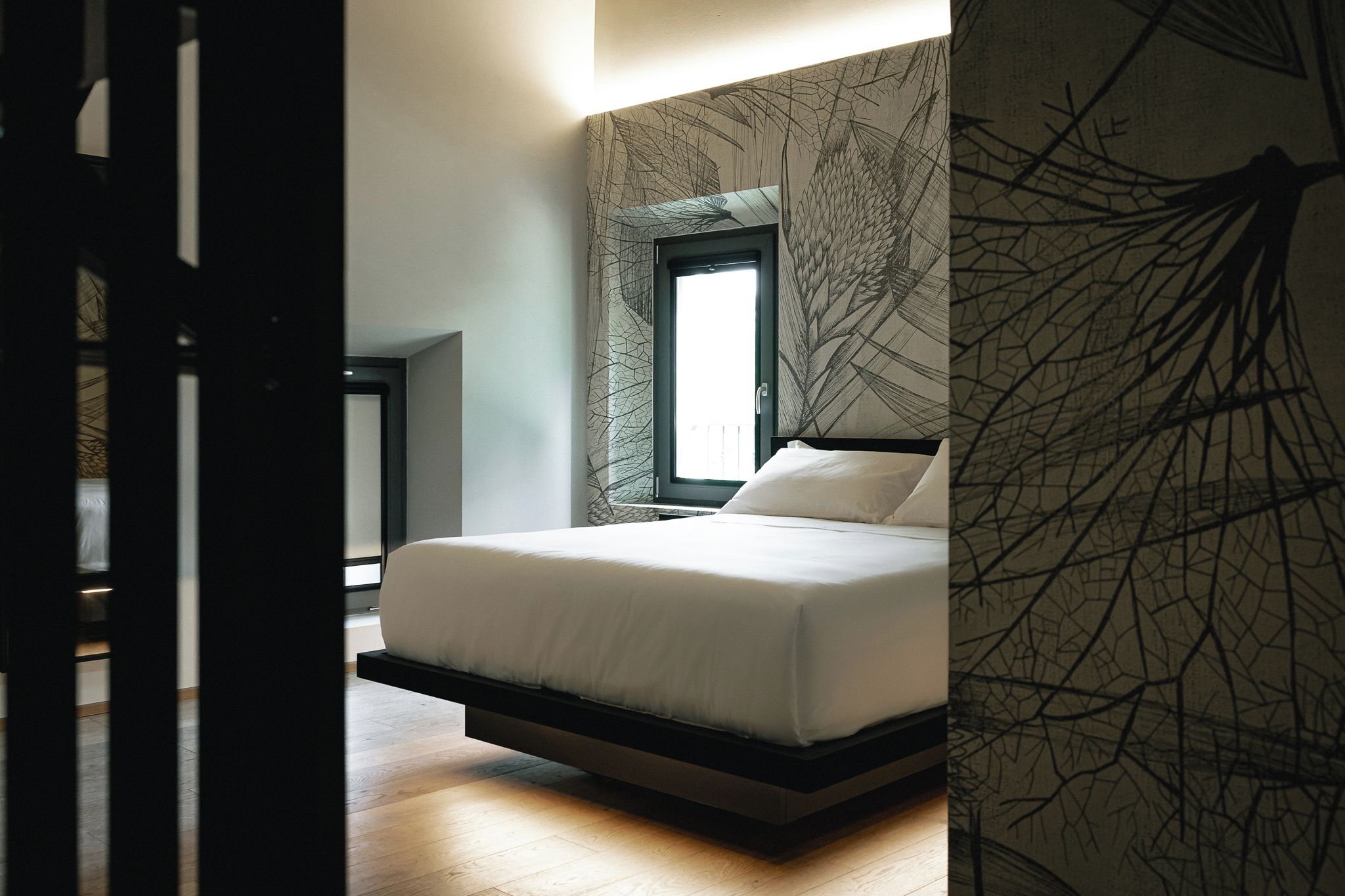 Ein modernes Schlafzimmer mit Bett, Fenster und Wand mit einem Astmuster.