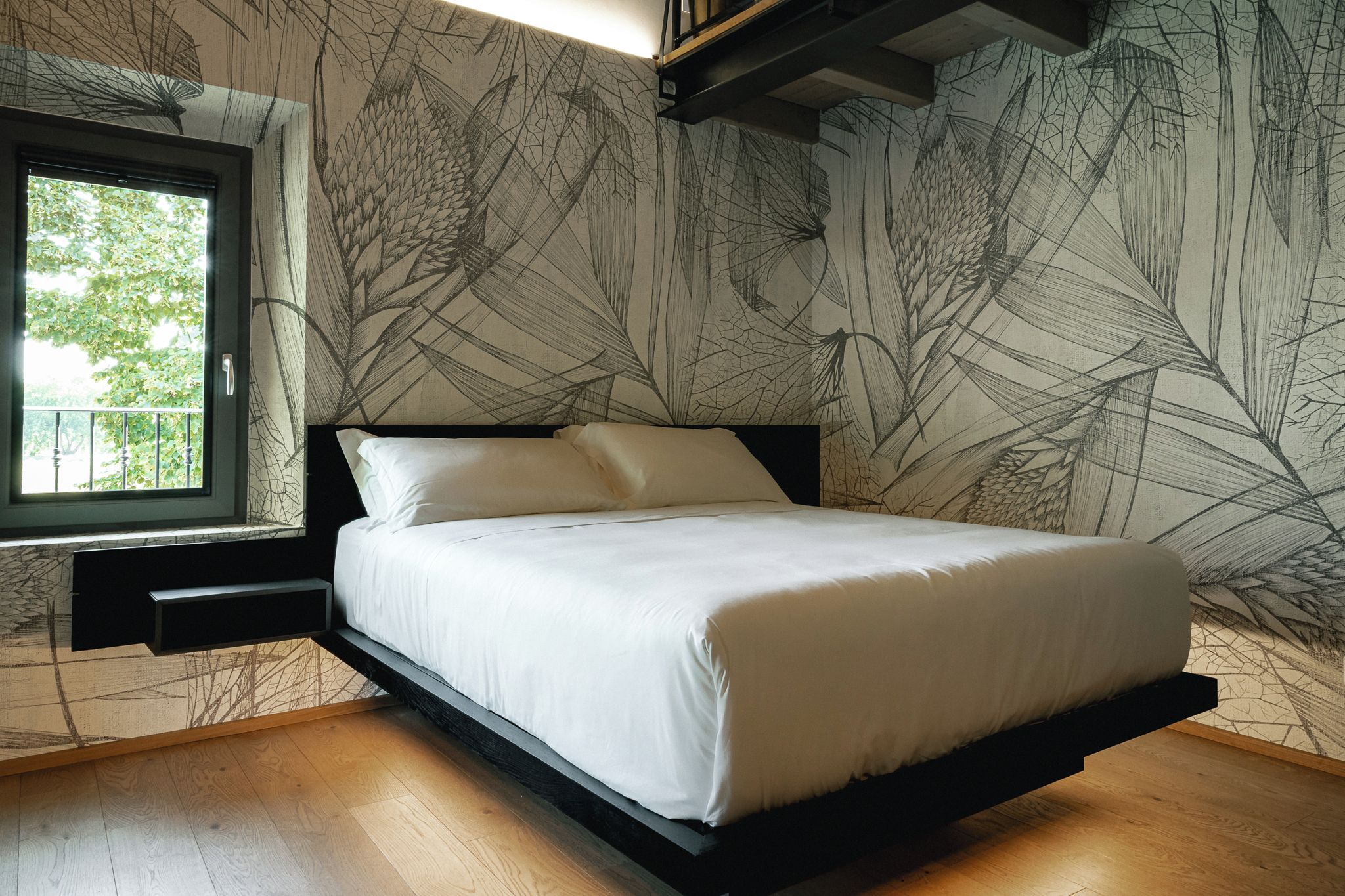 A modern bedroom with a bed, a window, and a wall with a leaf pattern.