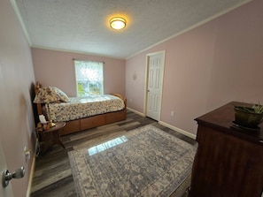 A bedroom with a bed, a nightstand, a lamp, a window with blinds, a door, and a rug.