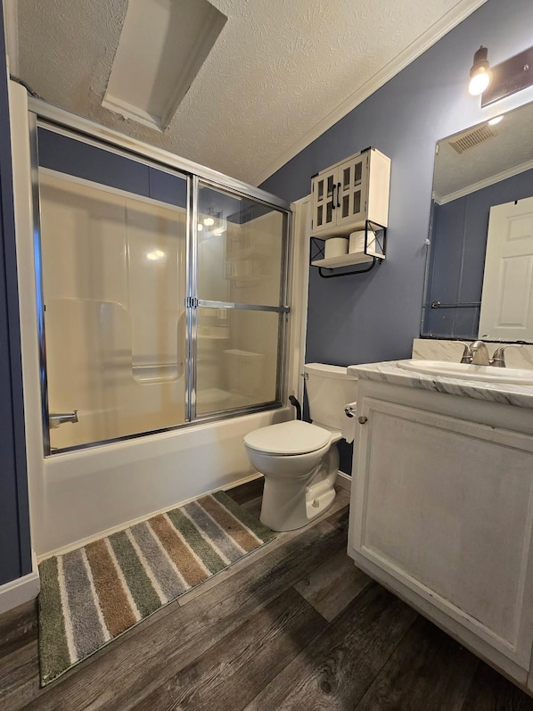 A bathroom with a glass-enclosed shower, a toilet, a sink with a marble countertop, and a mirror.