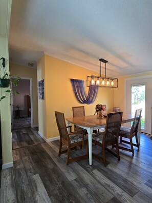 A dining area with a wooden table and chairs, a hanging light fixture, and a blue draped wall hanging.