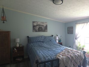 A bedroom with a bed, a nightstand, a lamp, a wall-mounted picture, and a window with curtains.
