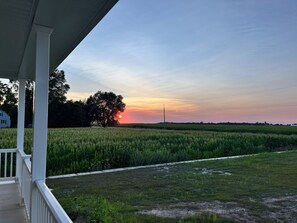 A rural landscape with a sunset, a field, and a house in the background.