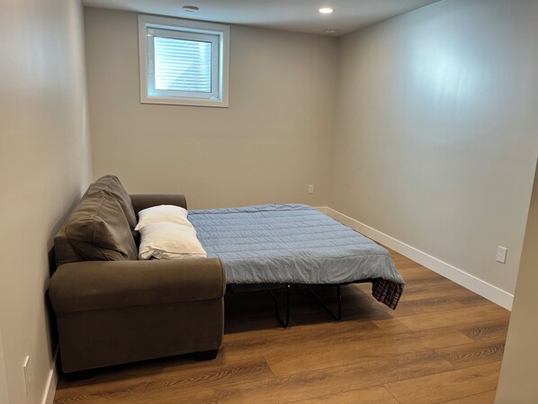A bedroom with a bed, a sofa, a window, and a ceiling light.