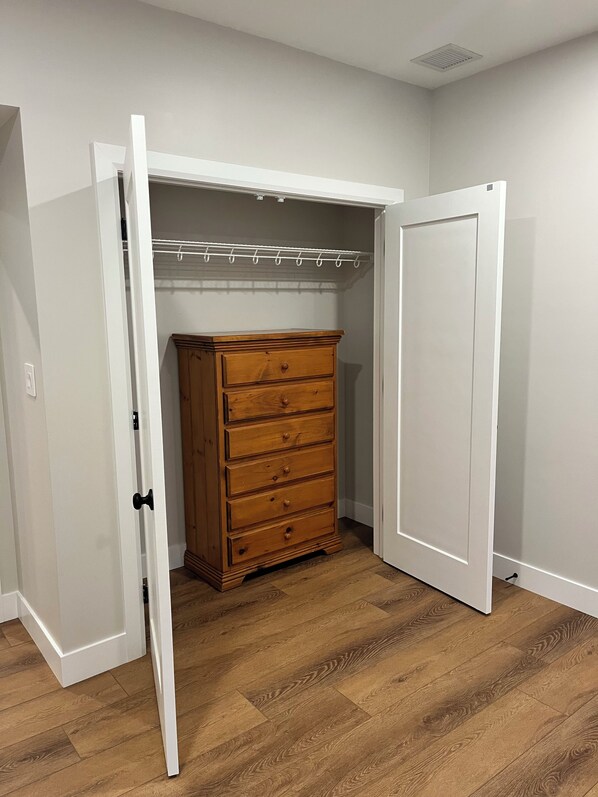 A room with a wooden dresser, a white closet with a hanging rod, and a white door.