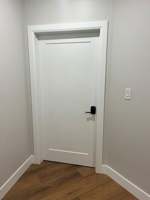 A white door with a black handle and a keyhole, set in a hallway with wooden flooring and white walls.