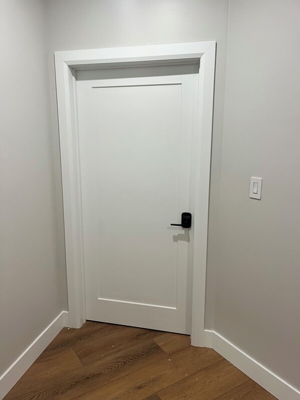 A white door with a black handle and a keyhole, set in a hallway with wooden flooring and white walls.
