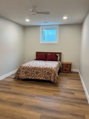 A bedroom with a bed, a nightstand, a ceiling fan, and a window.