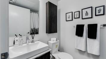 A modern bathroom with a white sink, toilet, and a large mirror. There are framed pictures on the wall and two towels hanging on a rack.