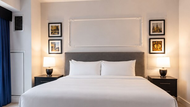Ein Hotelzimmer mit einem großen Bett, zwei Nachttischen mit Lampen und gerahmten Bildern an den Wänden.