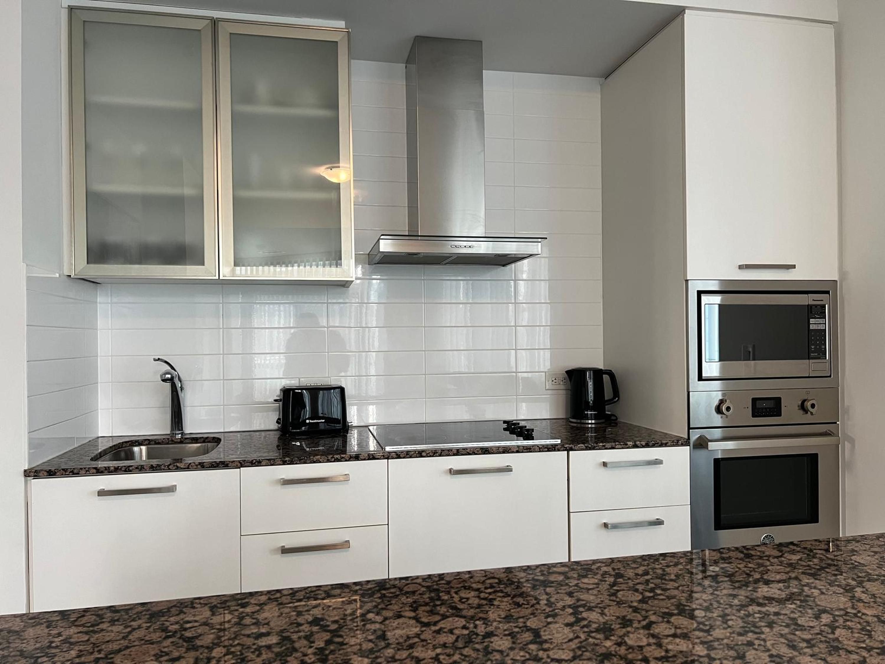 Una cocina moderna con armarios blancos, campana extractora de acero inoxidable, microondas integrado y cafetera.
