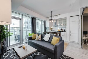 Un apartamento moderno con un sofá gris, una mesa de comedor y una zona de cocina.
