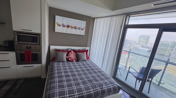 A hotel room with a bed, a kitchenette, and a large window with a city view. - Central Toronto Suites (Toronto)