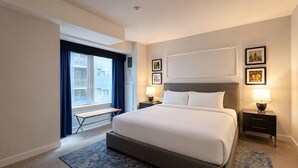Ein Hotelzimmer mit einem großen Bett, Nachttischen, einem Schreibtisch und einem Fenster mit Vorhängen.