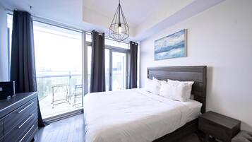Una habitación de hotel moderna con una cama grande, un tocador, una mesita de noche y un balcón con vistas a la ciudad.