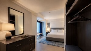 Ein Hotelzimmer mit Bett, Kommode, Spiegel, einer Bank und einem begehbaren Kleiderschrank.