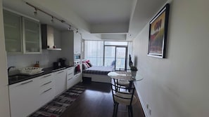 A compact kitchen with a dining area, a bed, and a large window with a city view. - Central Toronto Suites (Toronto)