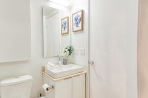 Een badkamer met toilet, wastafel, spiegel, een lijst met bloemen en een vaas met bloemen.