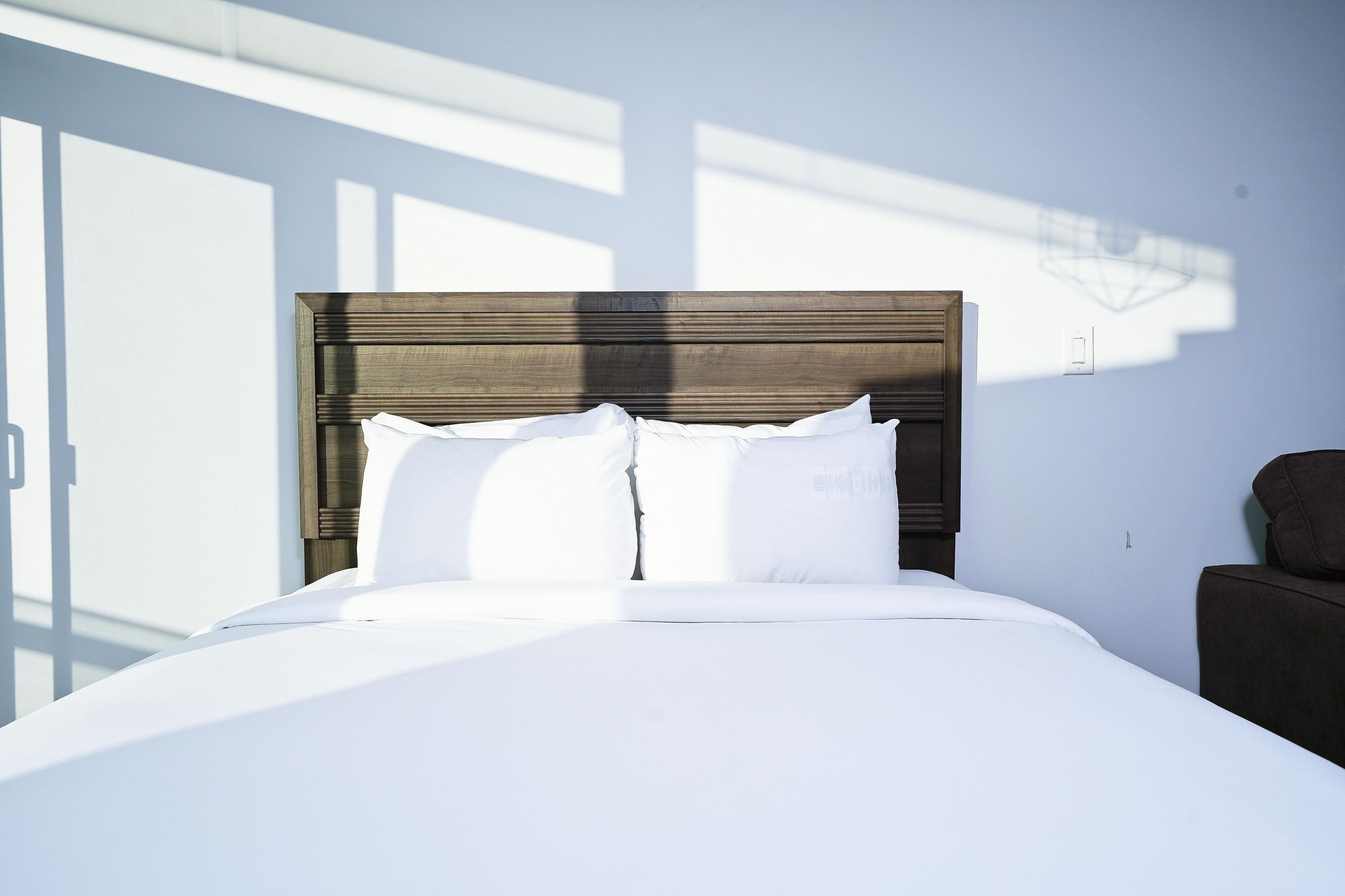Una cama bien tendida con sábanas blancas y un cabecero de madera en una habitación de hotel.