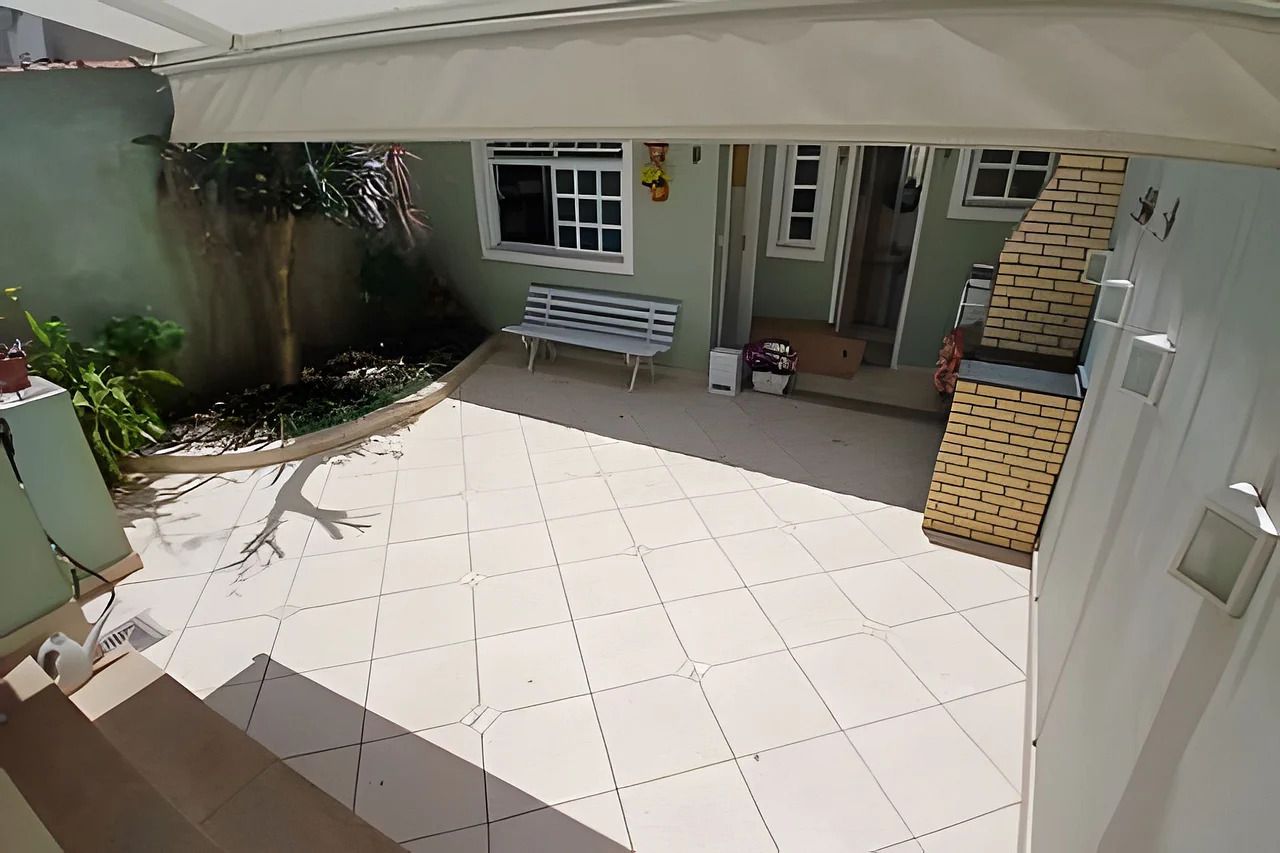 Un patio con baldosas, una banca, una pequeña zona ajardinada y una estructura de ladrillo.