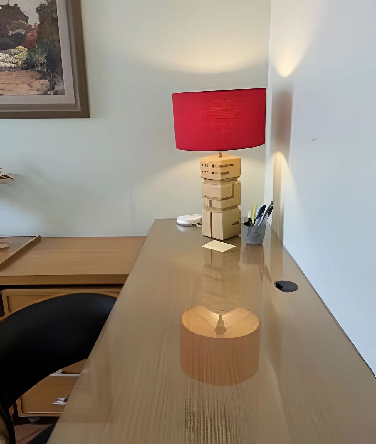 Un escritorio de madera con una lámpara roja, una pila de cajas y un pequeño recipiente con cubiertos.