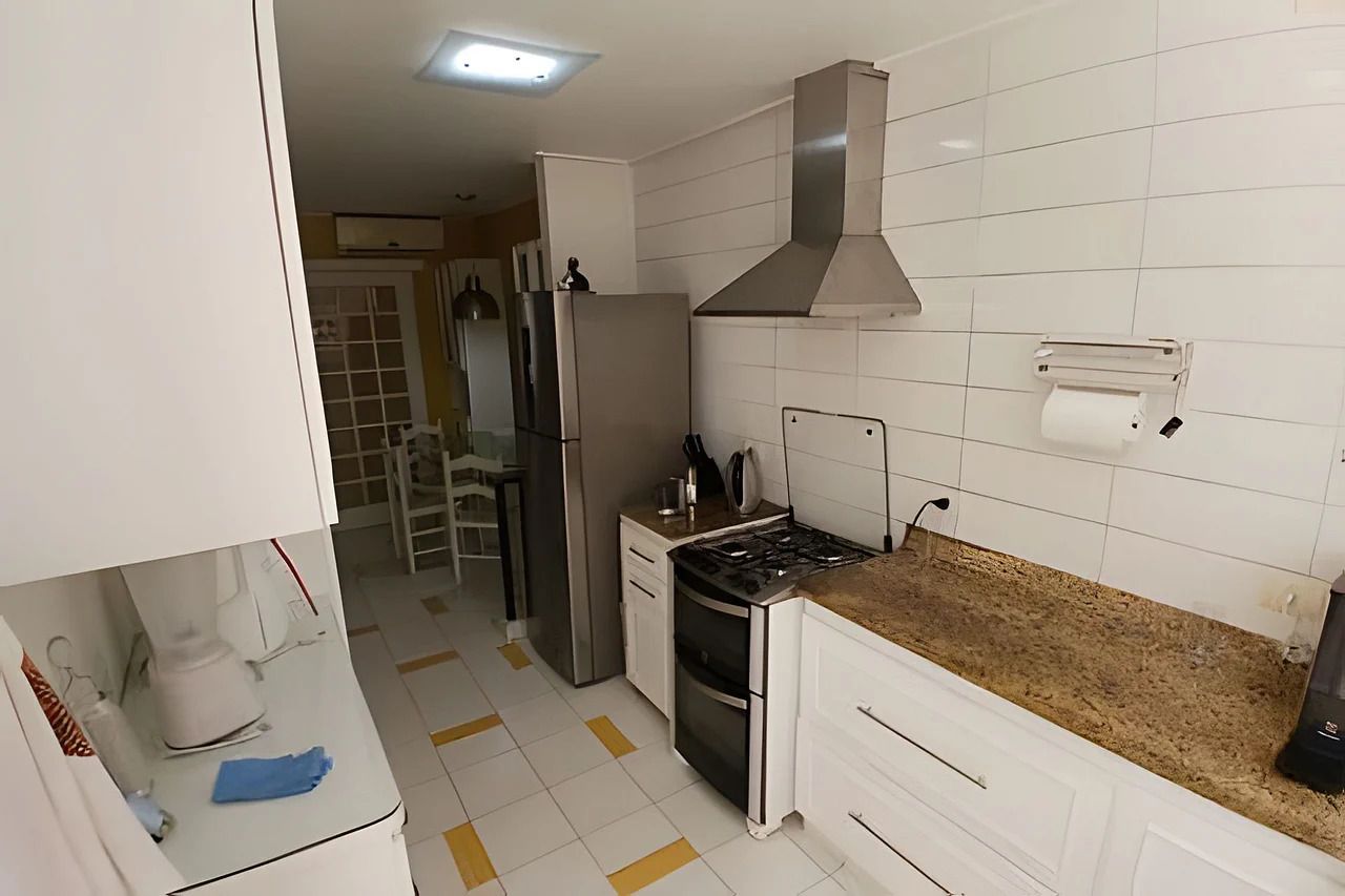 Una cocina con armarios blancos, un refrigerador de acero inoxidable, una estufa a gas y una campana extractora.