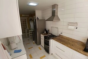 Una cocina con armarios blancos, un refrigerador de acero inoxidable, una estufa a gas y una campana extractora.