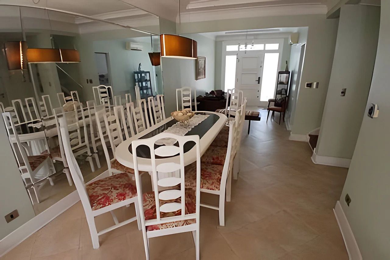Un comedor con una mesa redonda y sillas blancas, una araña y vista a otra habitación.