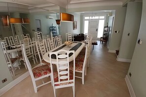 Un comedor con una mesa redonda y sillas blancas, una araña y vista a otra habitación.