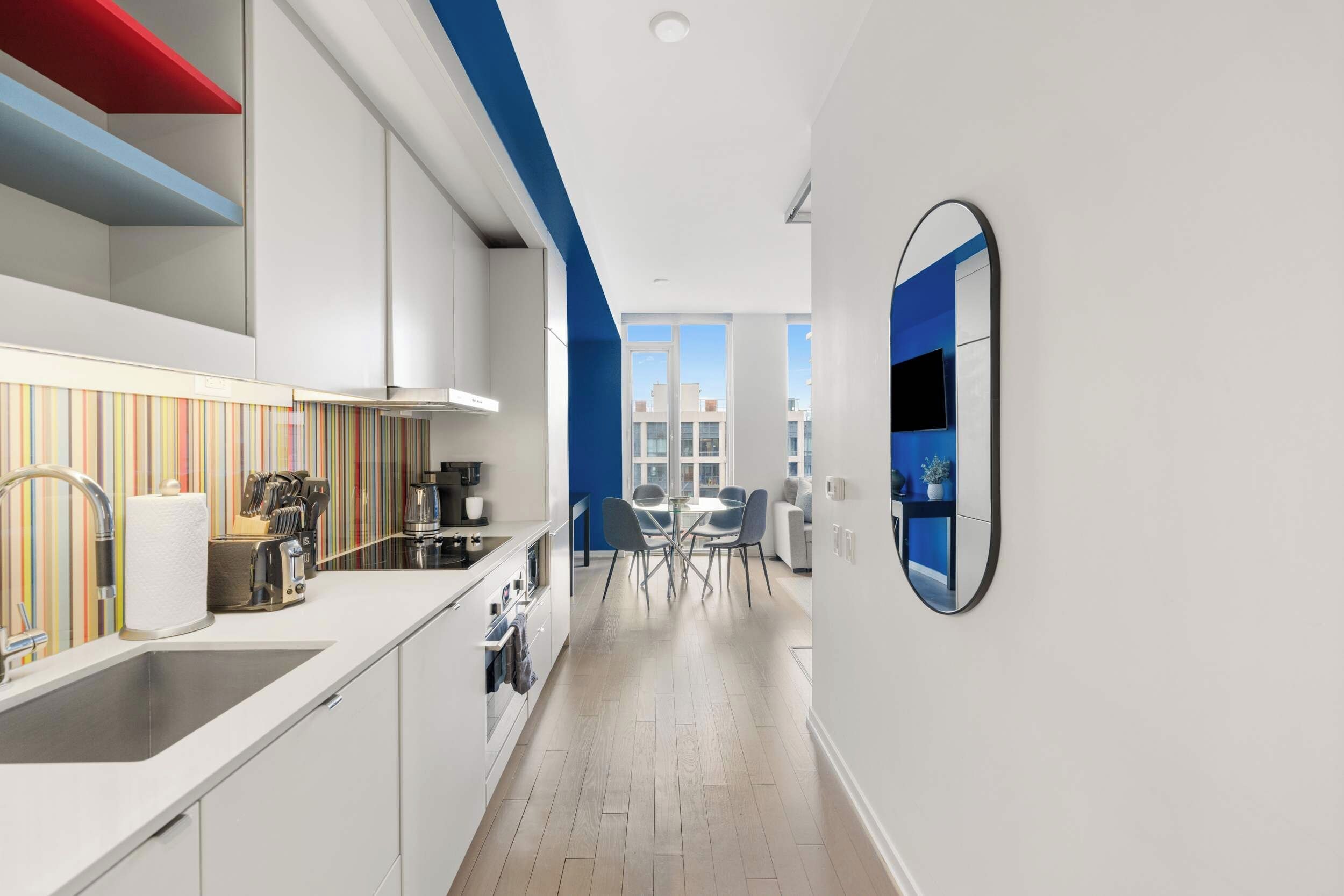 A modern kitchen with white cabinetry, a striped backsplash, and a view into the dining area.