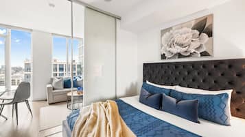 A modern bedroom with a large bed, a city view, and a dining area with a table and chairs.