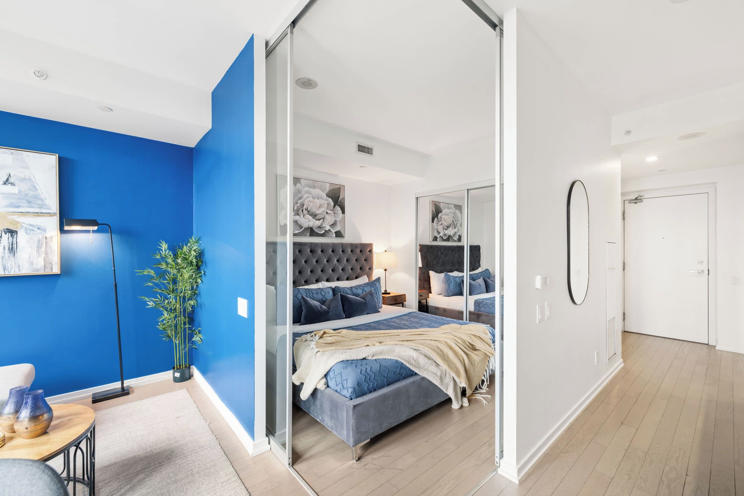 A modern bedroom with a blue accent wall, a large bed with a tufted headboard, and a glass partition.