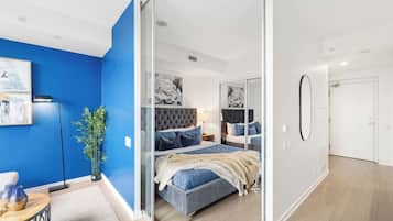 A modern bedroom with a blue accent wall, a large bed with a tufted headboard, and a glass partition.