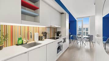 A modern kitchen with white cabinets, a striped backsplash, and a dining area with a blue accent wall and a glass table.