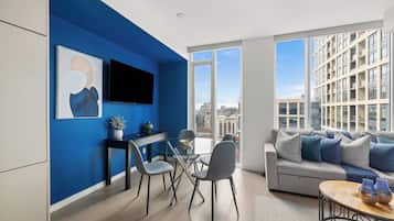 Una sala de estar moderna con una pared azul de acento, un televisor de pantalla plana, un comedor con mesa de vidrio y un sofá con cojines.