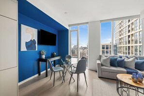 Ein modernes Wohnzimmer mit blauer Akzentwand, einem Flachbildfernseher, einem Essbereich mit Glastisch und einer Couch mit Kissen.