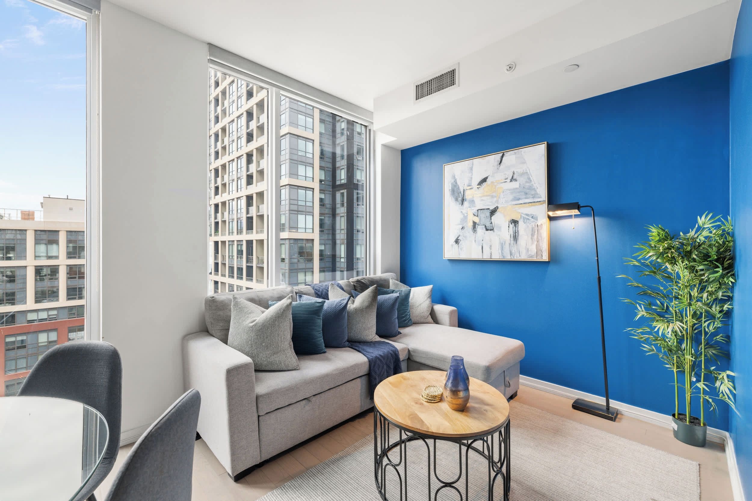 A modern living room with a grey sofa, a round wooden coffee table, and a blue accent wall.