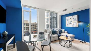 Una sala moderna con una mesa de comedor de cristal, sofás grises y una pared azul de acento.