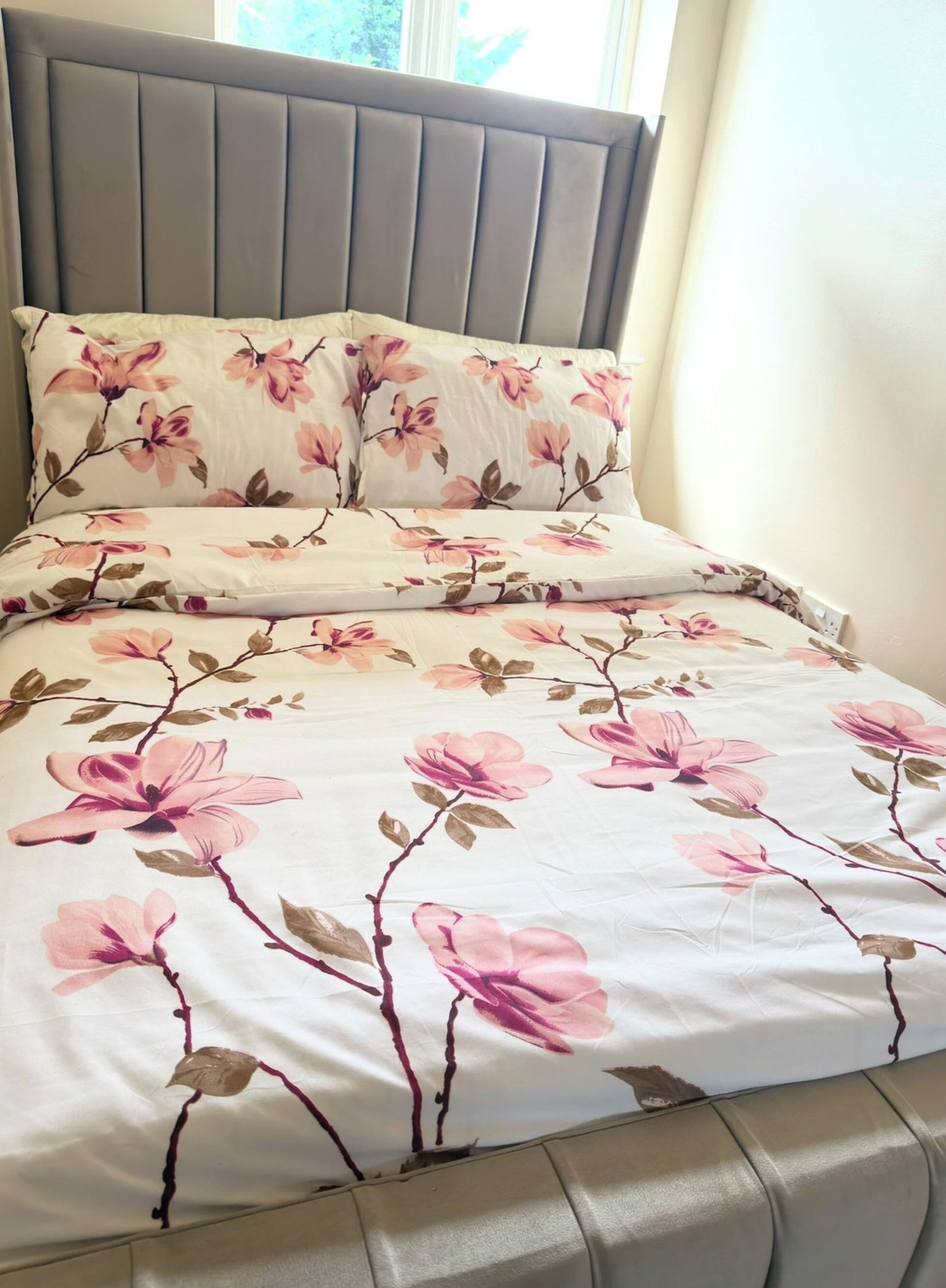 A bed with a floral bedspread and matching pillows, a padded headboard, and a window with daylight.