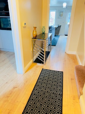 A hallway with a black patterned rug, a glass table with a vase, and a sofa in the background. - More Photos to Come in few Weeks (Norwich)