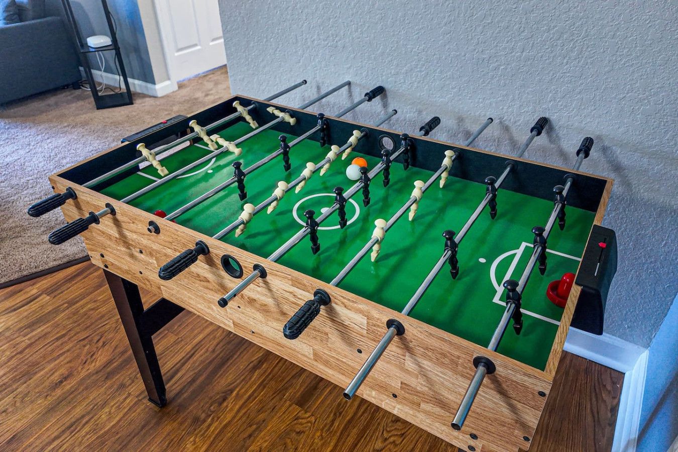 Una mesa de fútbol de madera con superficie de juego verde y varias barras con figuras.