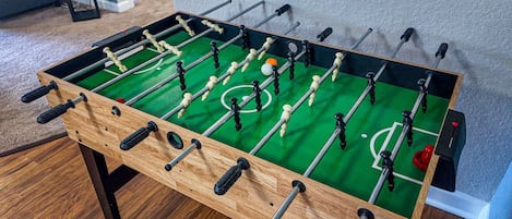 Una mesa de fútbol de madera con superficie de juego verde y varias barras con figuras.