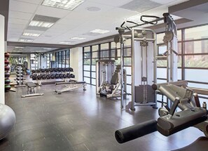 Un gimnasio con diverso equipo de ejercicio, incluyendo mancuernas, una banca y una máquina de poleas.