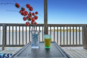 A wooden deck with a glass table, a vase with red flowers, and a glass of yellow liquid. - Waterfront Oasis Bay Views near NASA & Kemah (Seabrook)