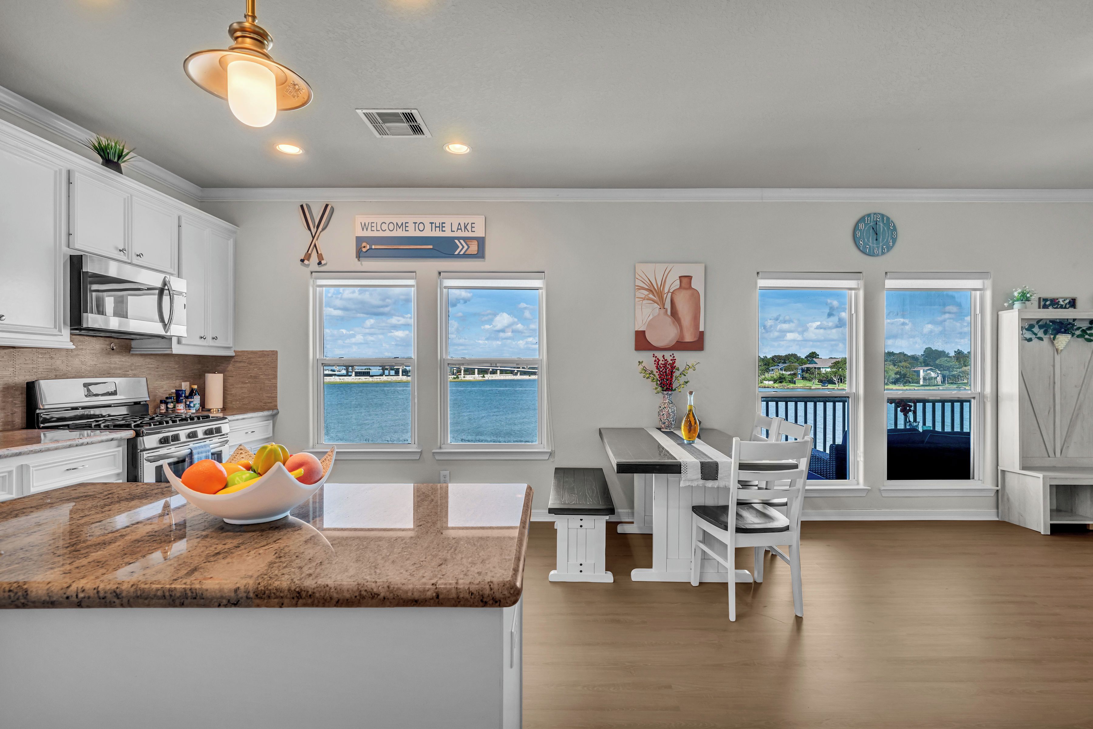A modern kitchen with a large island, a dining area with a view of the lake, and a sign welcoming visitors to the lake.