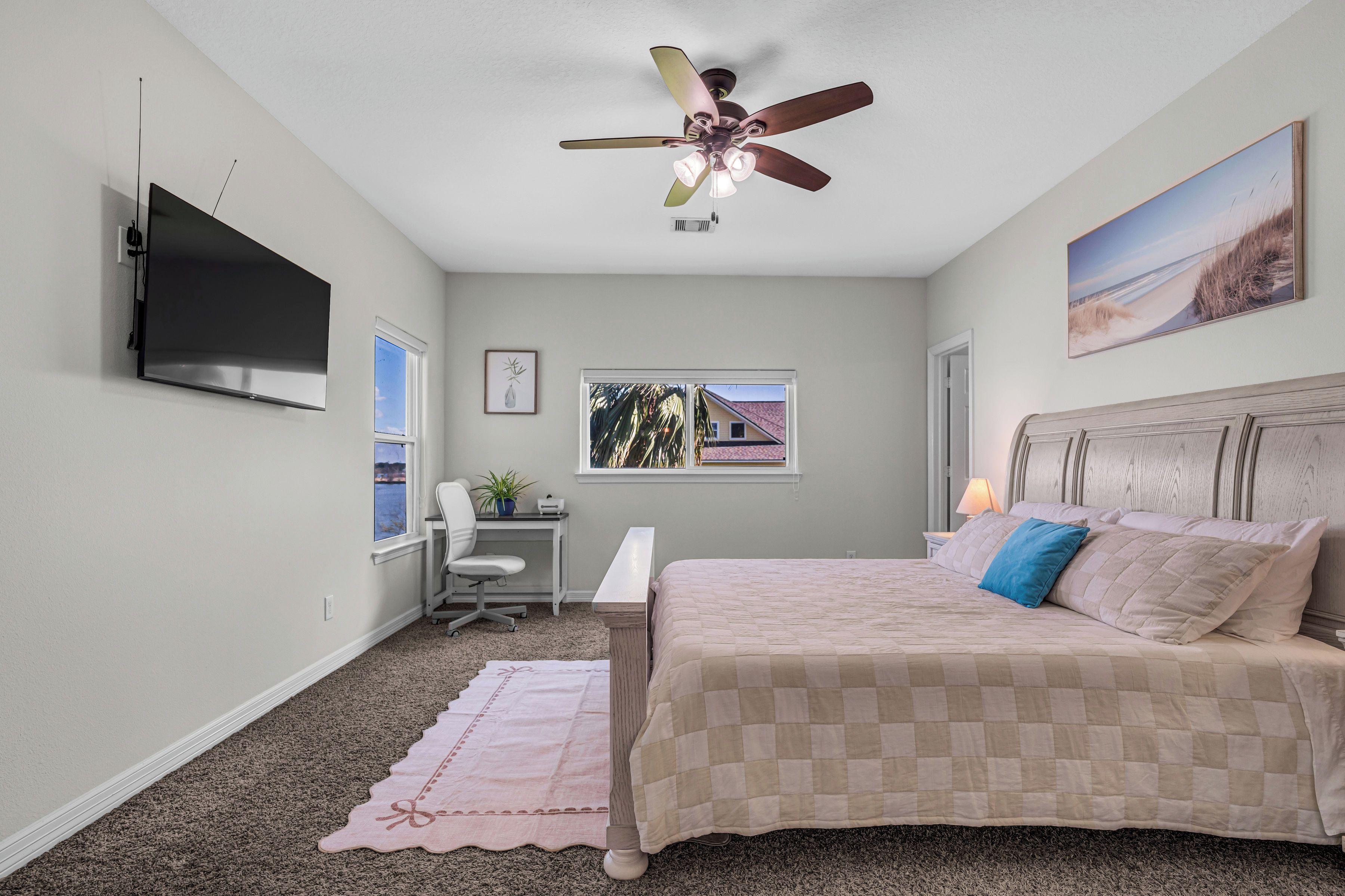 Une chambre à coucher comprenant un lit, un bureau, une chaise, une télévision, un ventilateur de plafond et une fenêtre donnant sur un paysage agréable.