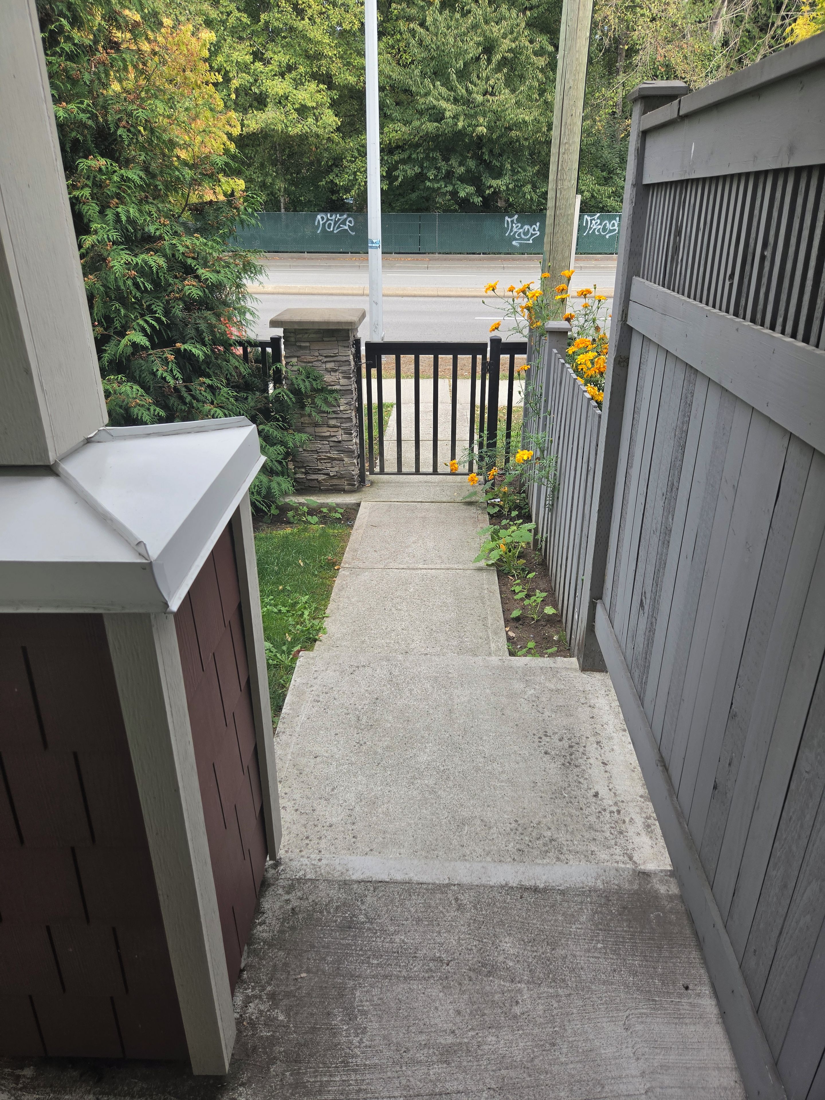A concrete pathway leading to a gated area with a stone wall and a wooden fence.