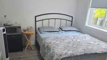 A bedroom with a bed, a wall clock, a bedside table with a lamp, and a window.